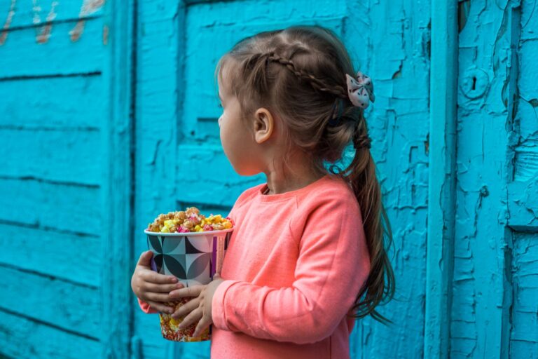 Una bambina che mangia popcorn zuccherati in un ambiente fatiscente: metafora dei diversi fattori di rischio per l'obesità infantile e punto di partenza a degli interventi scuola-famiglia